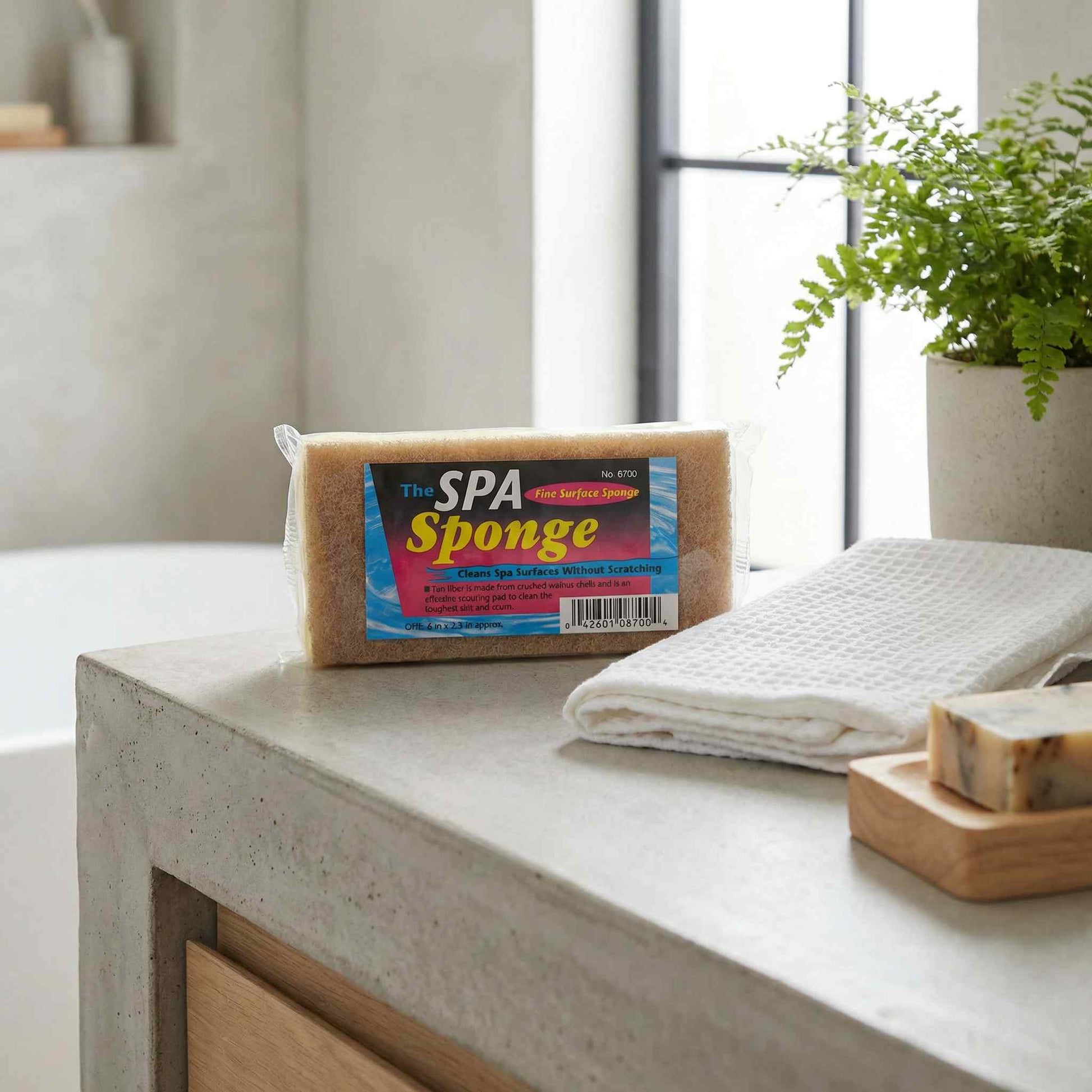Spa Sponge in packaging on a counter with towels and river stones in a spa-style bathroom